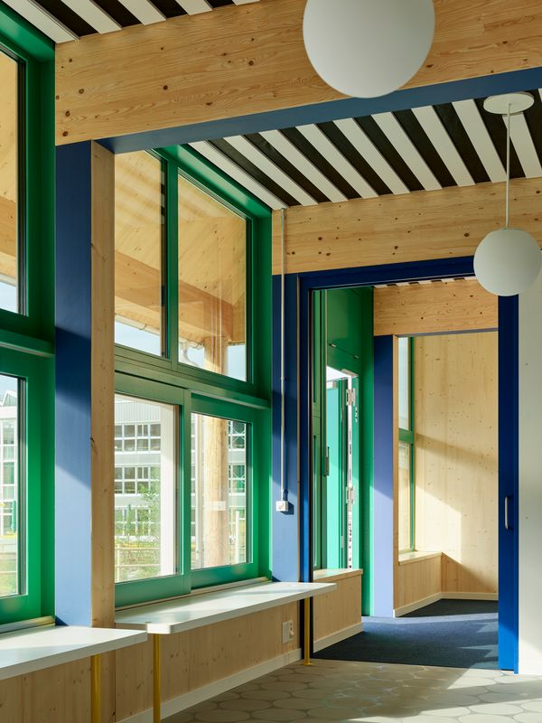 Areal Guggach – Die Kindergartenkinder blicken aus dem eingeschossigen, hölzernen Pavillon erwartungsvoll auf ihre Schulzeit im benachbarten Primarschulhaus. Verschiedene Stationen der Lernbiografie sind nur einen Steinwurf voneinander entfernt und haben doch jeweils ganz eigenständige, altersgerechte Räume zur Aneignung. – Philip Heckhausen